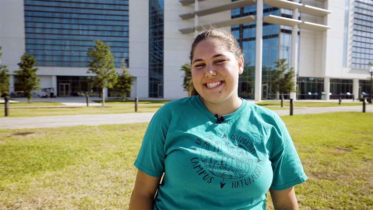 A woman in a green t-shirt stands outdoors in front of The Water School building