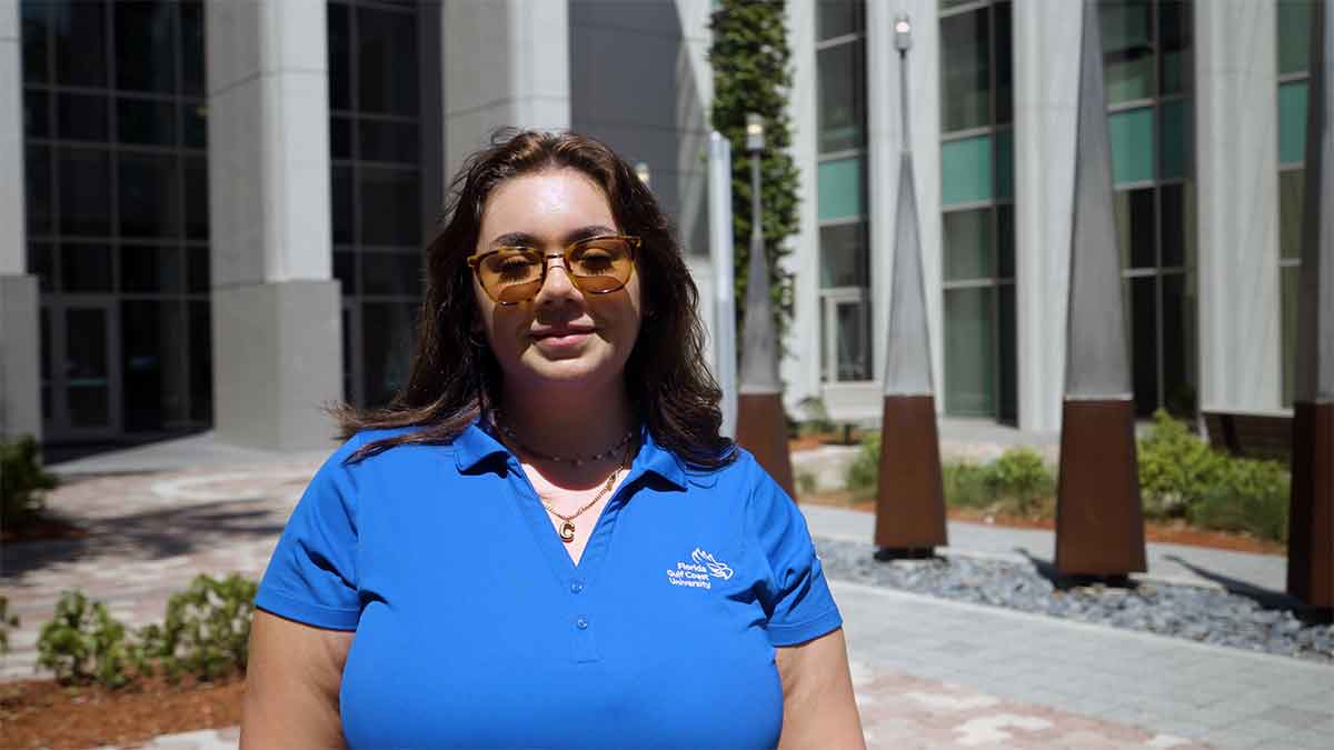 A woman in sunglasses and a blue, V-neck polo stands outdoors