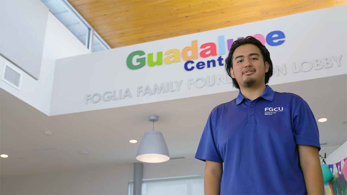A man in a blue polo shirt stands indoors in front of a sign that reads Guadalupe Center
