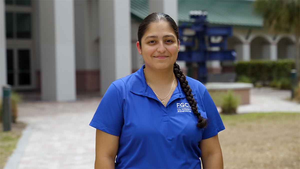 A woman in a blue polo shirt with her hair pulled into one braided ponytail stands outdoors
