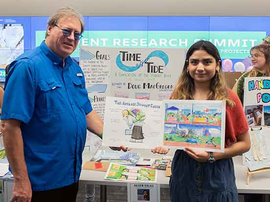 A man in a blue button-down shirt and a young woman in a denim skirt and red shirt. She is holding two cartoons, one is of a hunched over college student with a heavy backpack