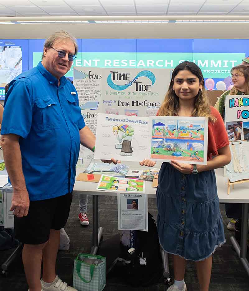 A man in a blue button-down shirt and a young woman in a denim skirt and red shirt. She is holding two cartoons, one is of a hunched over college student with a heavy backpack
