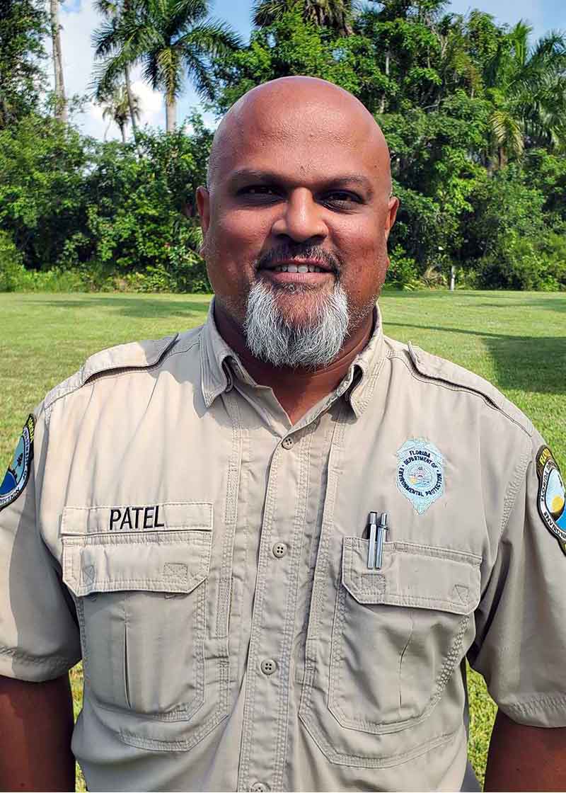 A headshot of a man in a beige button-down shirt with Patel on a label
