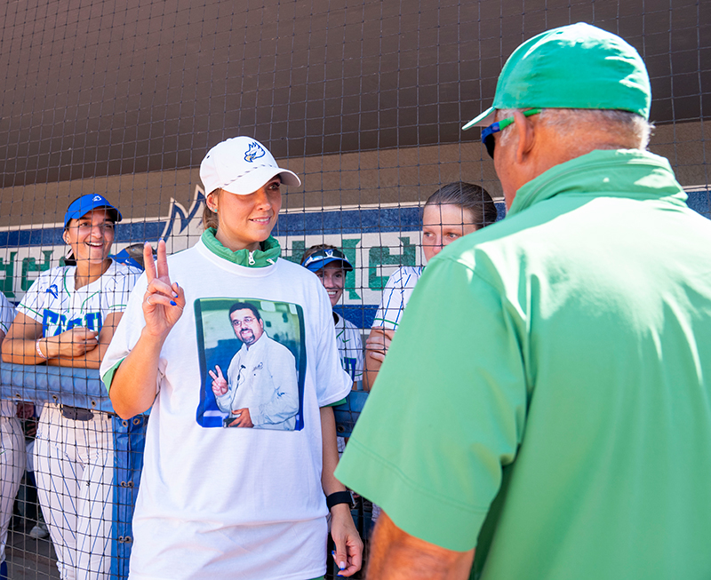 Woman in white T-shirt making peace sign at her softball coach