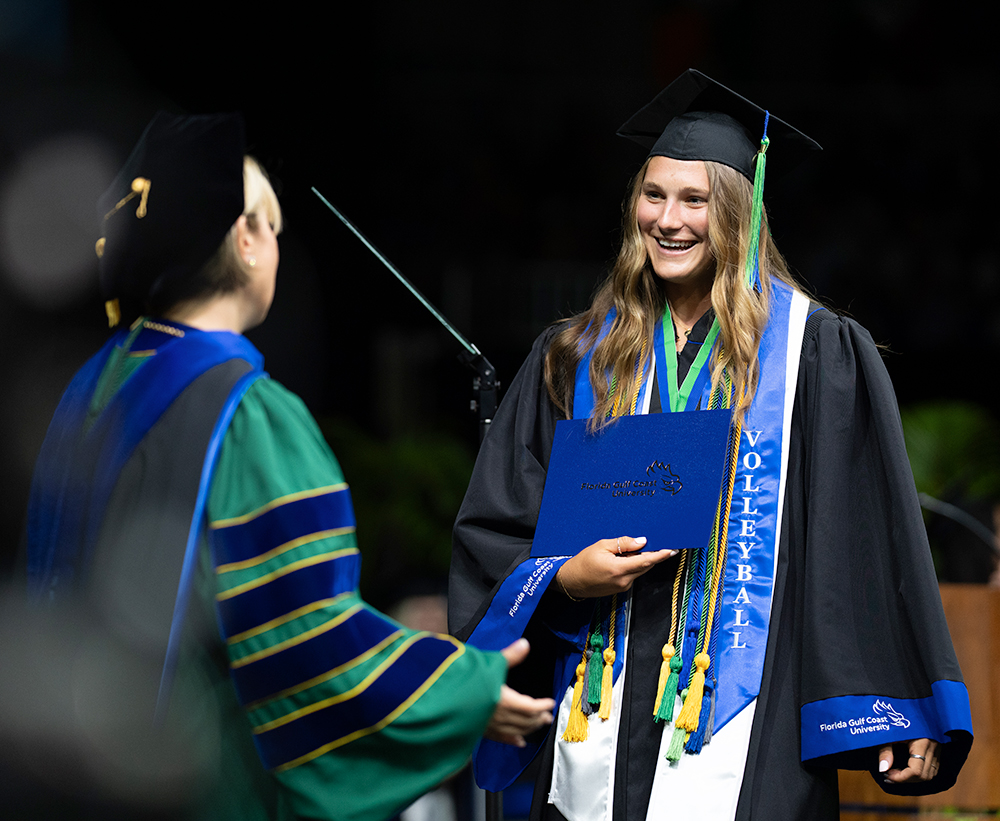 Woman in regalia handing diploma to woman in graduation cap and gown