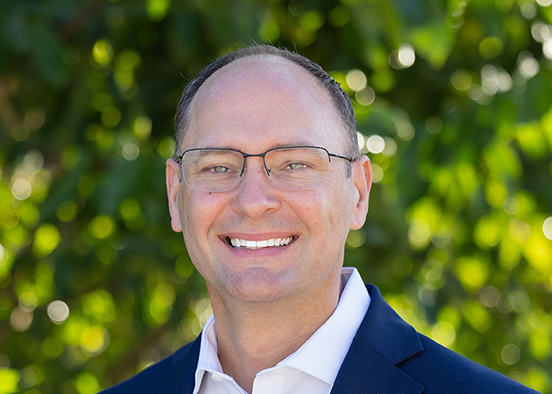 Man in blue blazer and white shirt wearing glasses and smiling