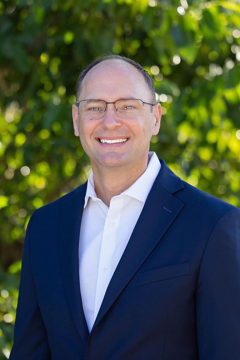 Man in blue blazer and white shirt wearing glasses and smiling