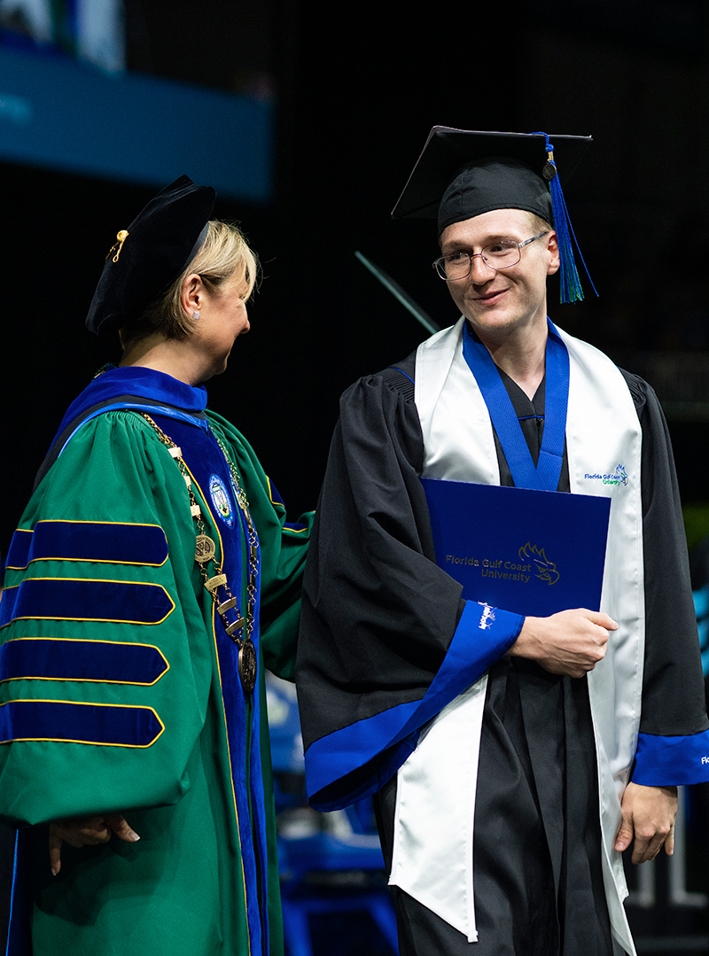 Woman in academic regalia congratulating man in graduation cap and gown during commencement.