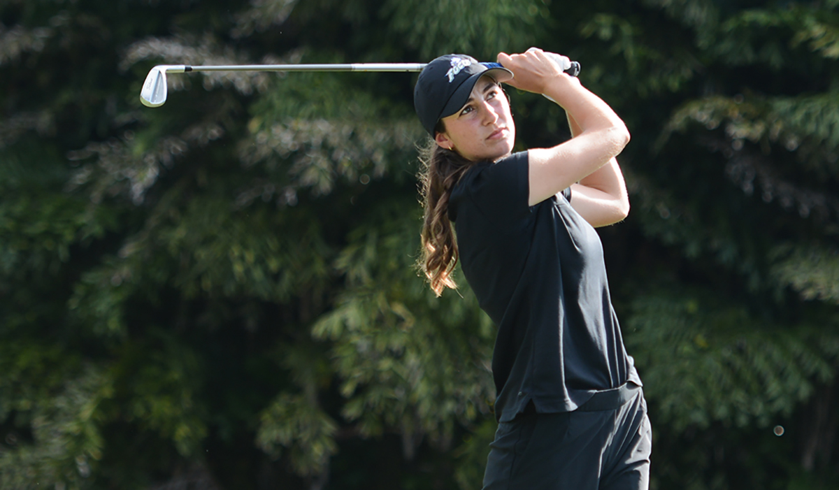Woman in black top and pants swinging golf club on course