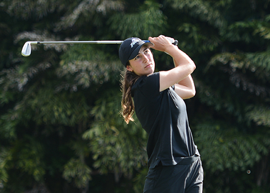Woman in black top and pants swinging golf club on course