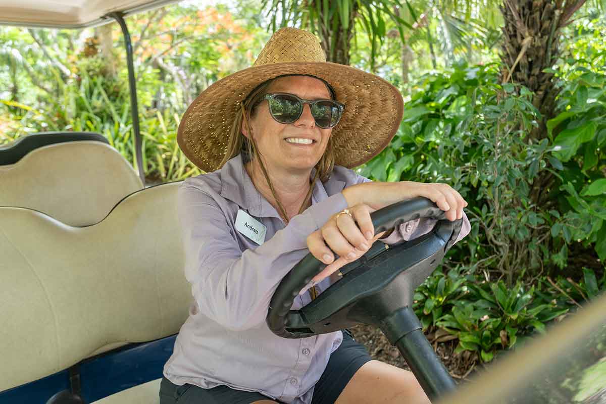A smiling woman in a sun hat and sunglasses driving a golf cart