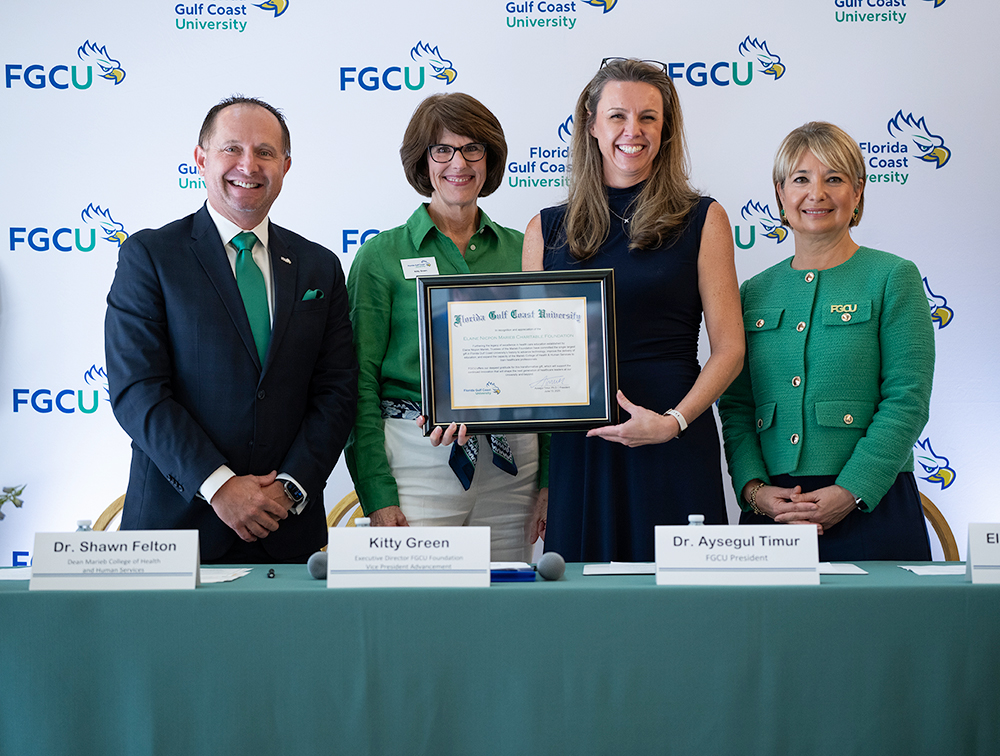 Four individuals stand in front of an FGCU backdrop smiling
