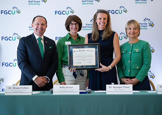 Four individuals stand in front of an FGCU backdrop smiling