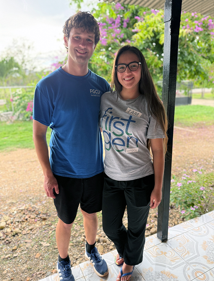 A man in a blue T-shirt and black shorts stands next to a woman in a gray T-shirt and black pants in a courtyard
