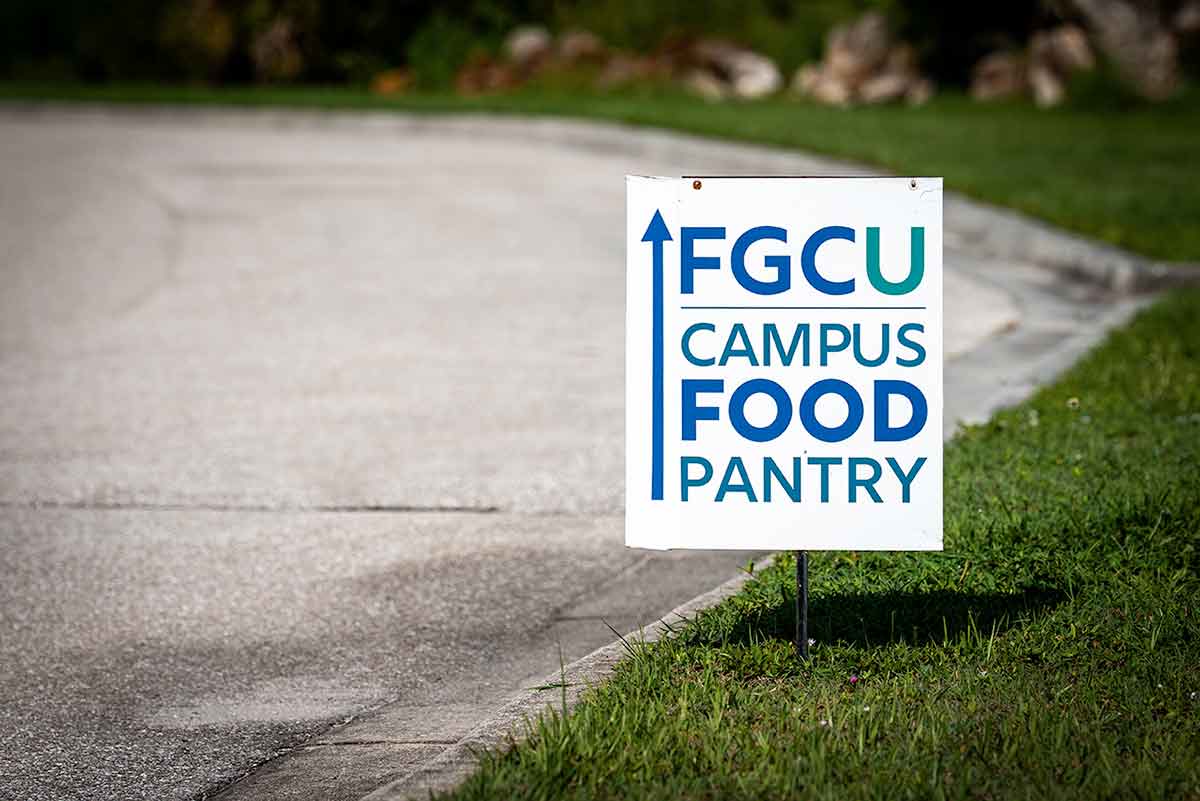A sign reads FGCU Campus Food Pantry and features a blue arrow pointing ahead on a road