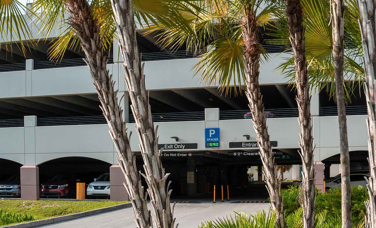 A parking garage entrance-exit is seen beyond a short driveway and several palm trees
