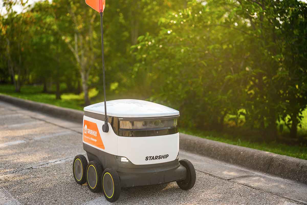 A white cooler on wheels with a small, red flag rolls by on a sidewalk