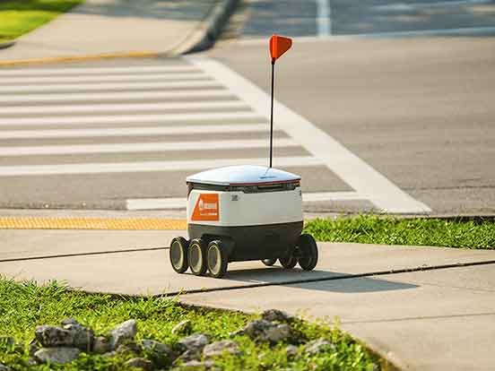 A white cooler on wheels with a small, red flag rolls by on a sidewalk