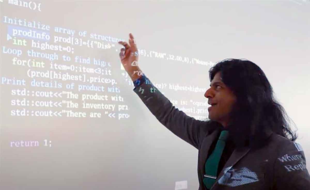 A long-haired man stands in front of a whiteboard with writing on it