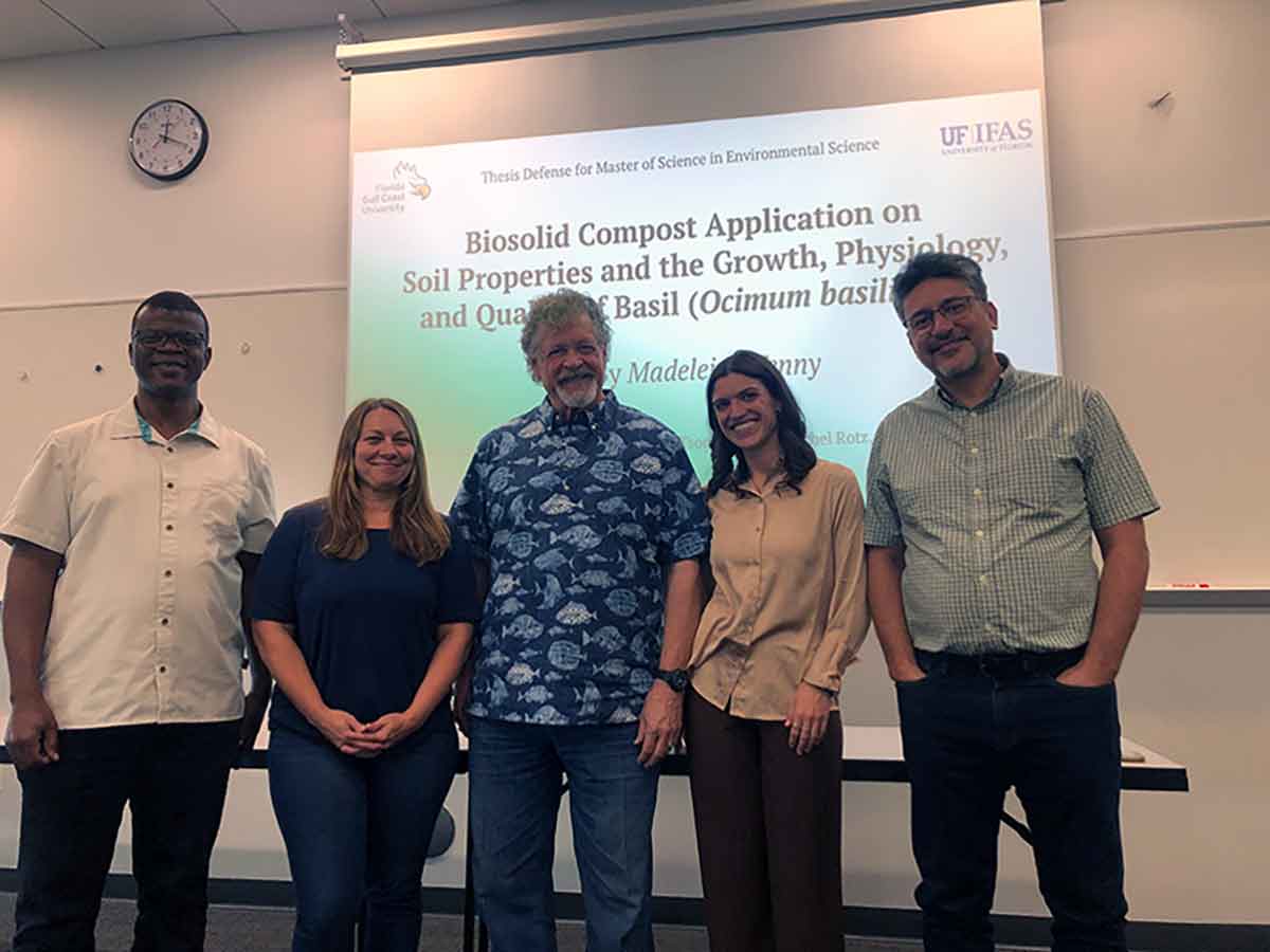Five people stand in front of a white board with a presentation slide that reads, Biosolid Compost Application on Soil Properties and the Growth, Physiology, and Quality of Basil
