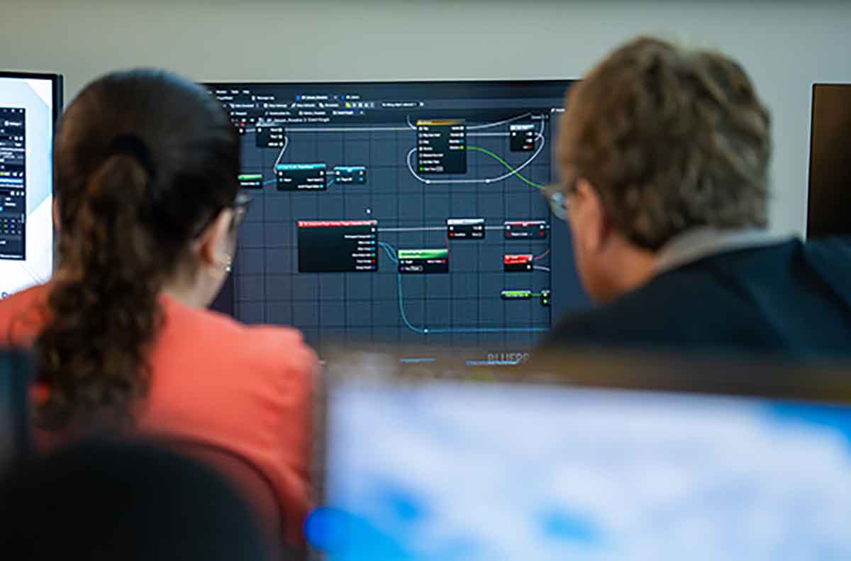 Two people viewing a computer screen displaying a visual programming interface with connected nodes