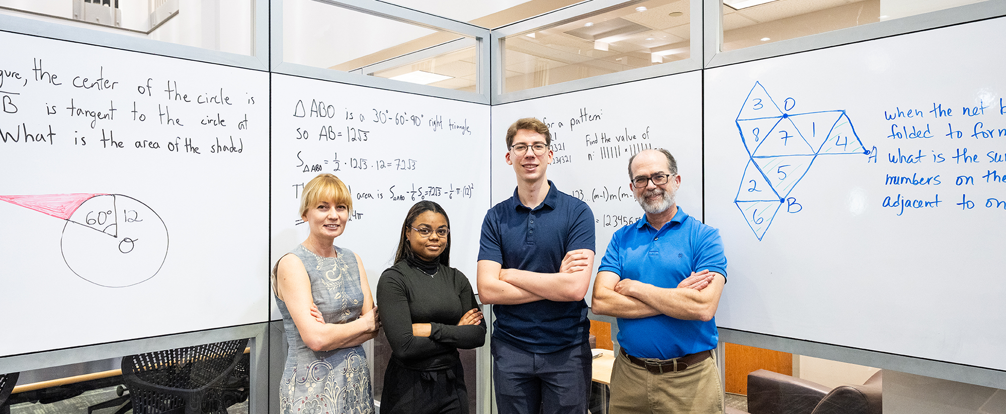 Four individuals stand in front of a whiteboard filled with mathematical equations and geometry problems. The group is posed with arms crossed, and the whiteboard displays triangle area calculations, algebraic expressions, and number theory formulas.
