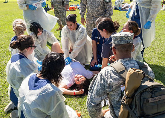 Group of responders surrounds person lying on grass during emergency training drill.