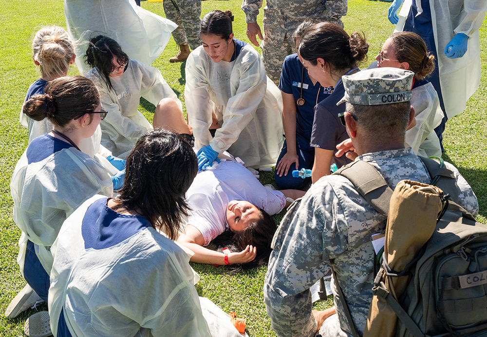 Group of responders surrounds person lying on grass during emergency training drill.