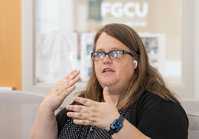 Person gesturing with hands during discussion in FGCU office, wearing smartwatch and earbuds.