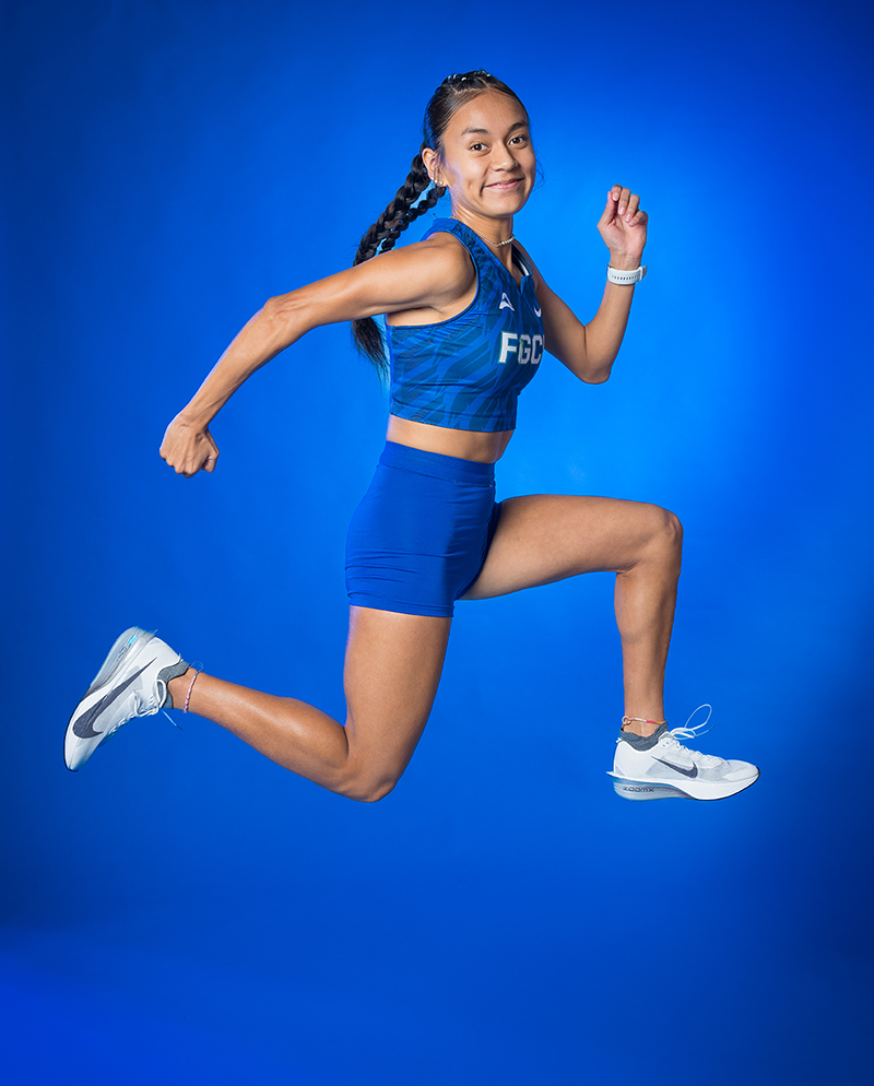 Athlete in FGCU uniform mid-air against a solid blue background.