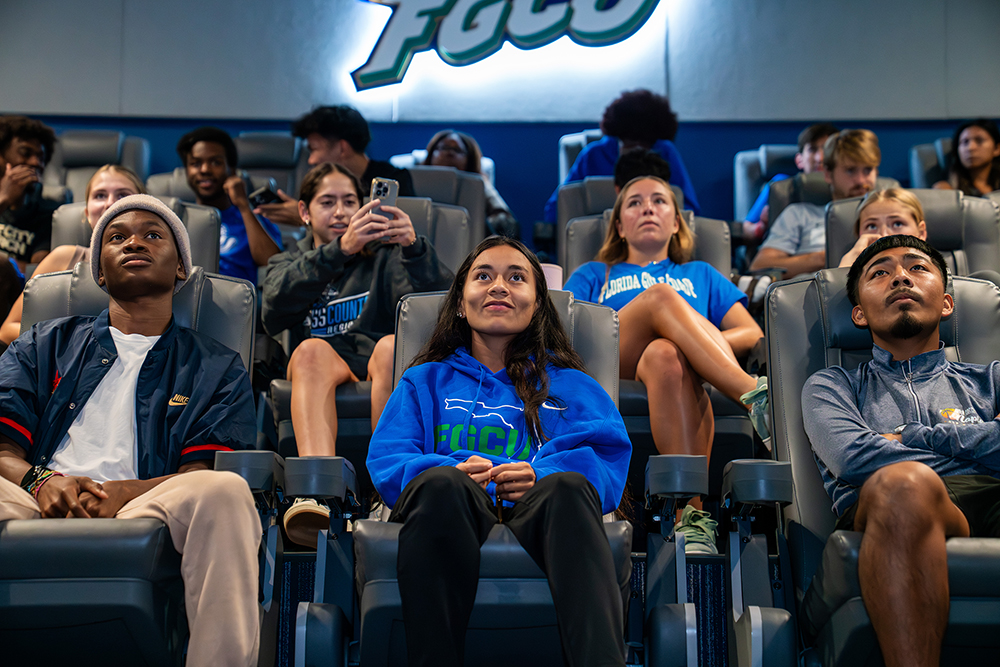 Students seated in a sports theater with tiered chairs and school branding.