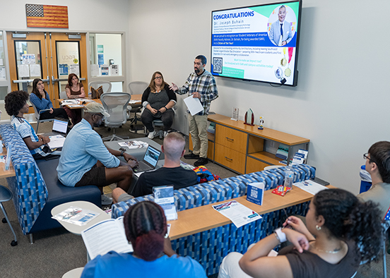 Group meeting in FGCU office with presentation screen displaying congratulations message
