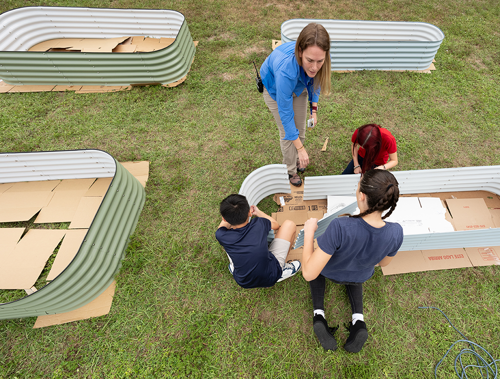 Group assembling metal garden beds on grass using cardboard as a base layer