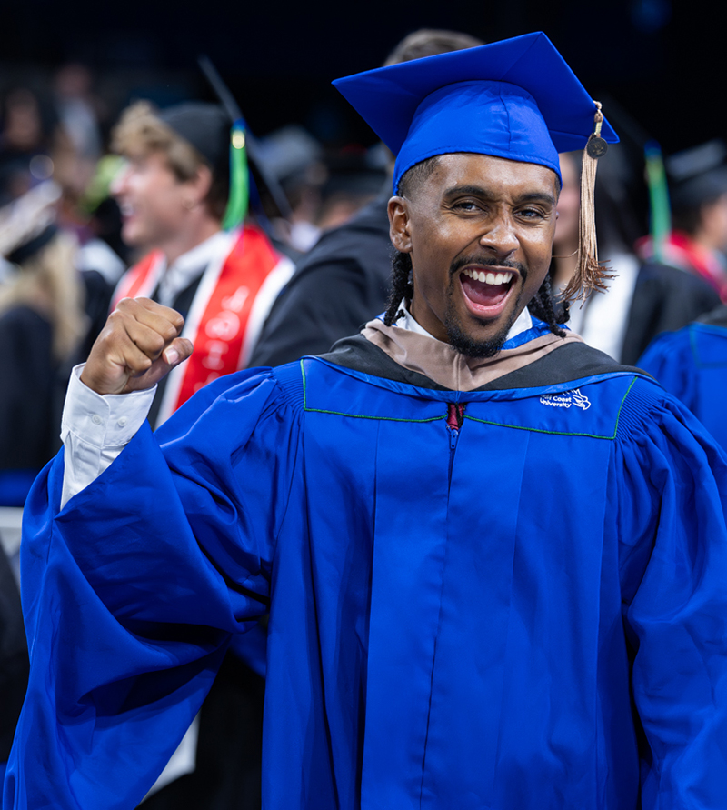 Graduate in a blue cap and gown raises a clenched fist during a commencement ceremony.