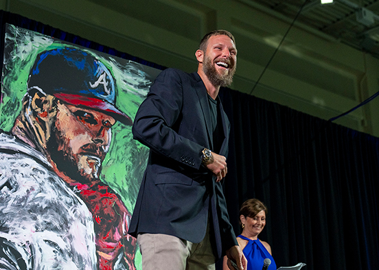 Person stands near a colorful painting of a baseball player during an auction event.
