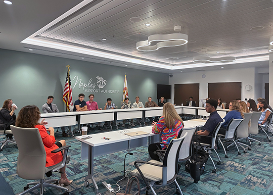 People seated around a U-shaped conference table at Naples Airport Authority during a meeting.