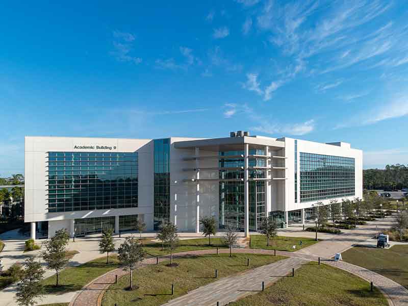 A drone photo of a multi-story building with lots of glass windows and a blue sky in the background. The words Academic Building 9 appear on the building