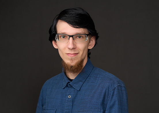 Person wearing a blue button-up shirt posed against a dark studio background.
