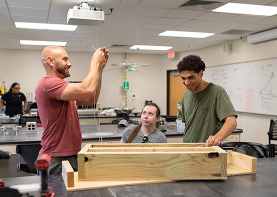 Students work together in a lab as one prepares wiring above a wooden beam mold