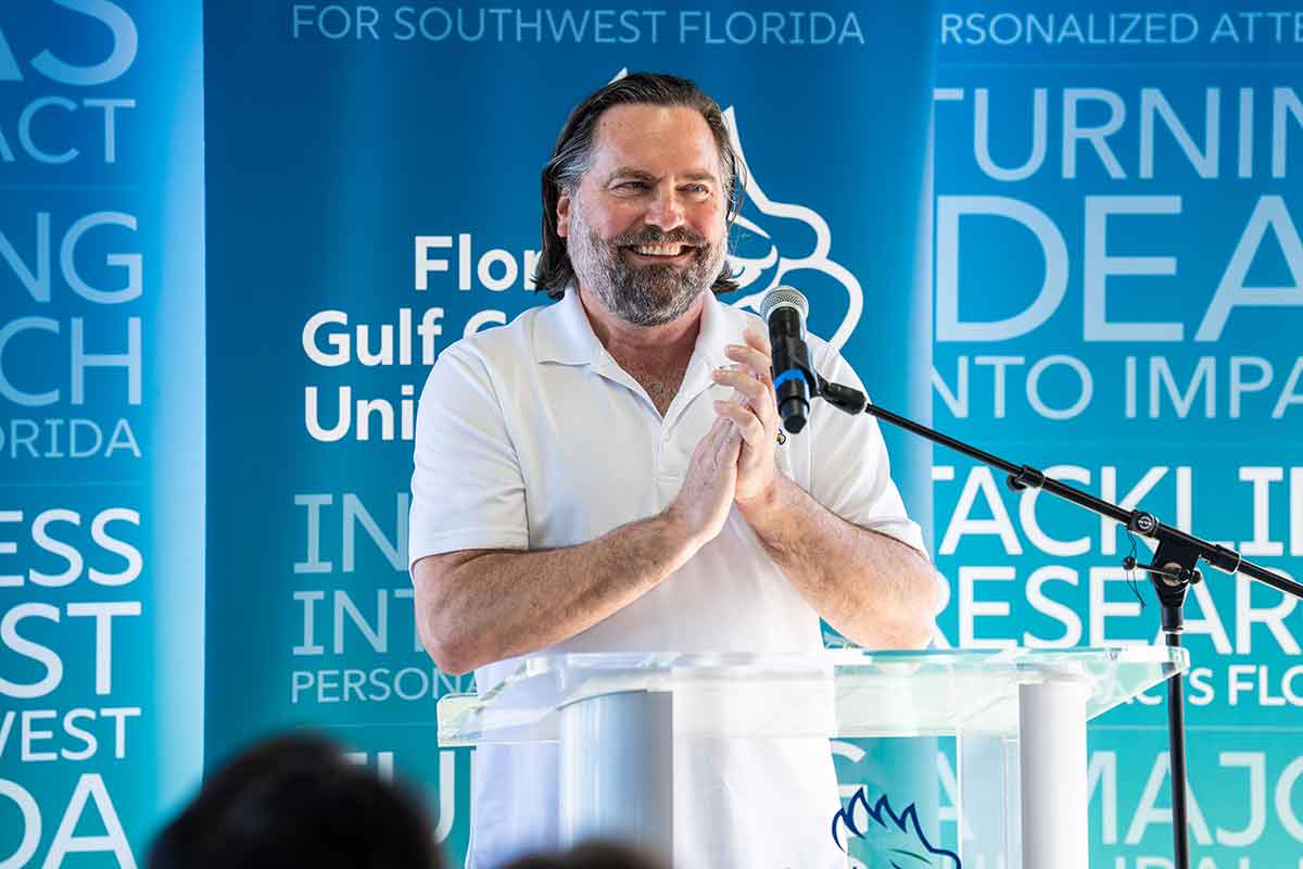 A man in a white beach button-up shirt stands in front of an FGCU step-and-repeat