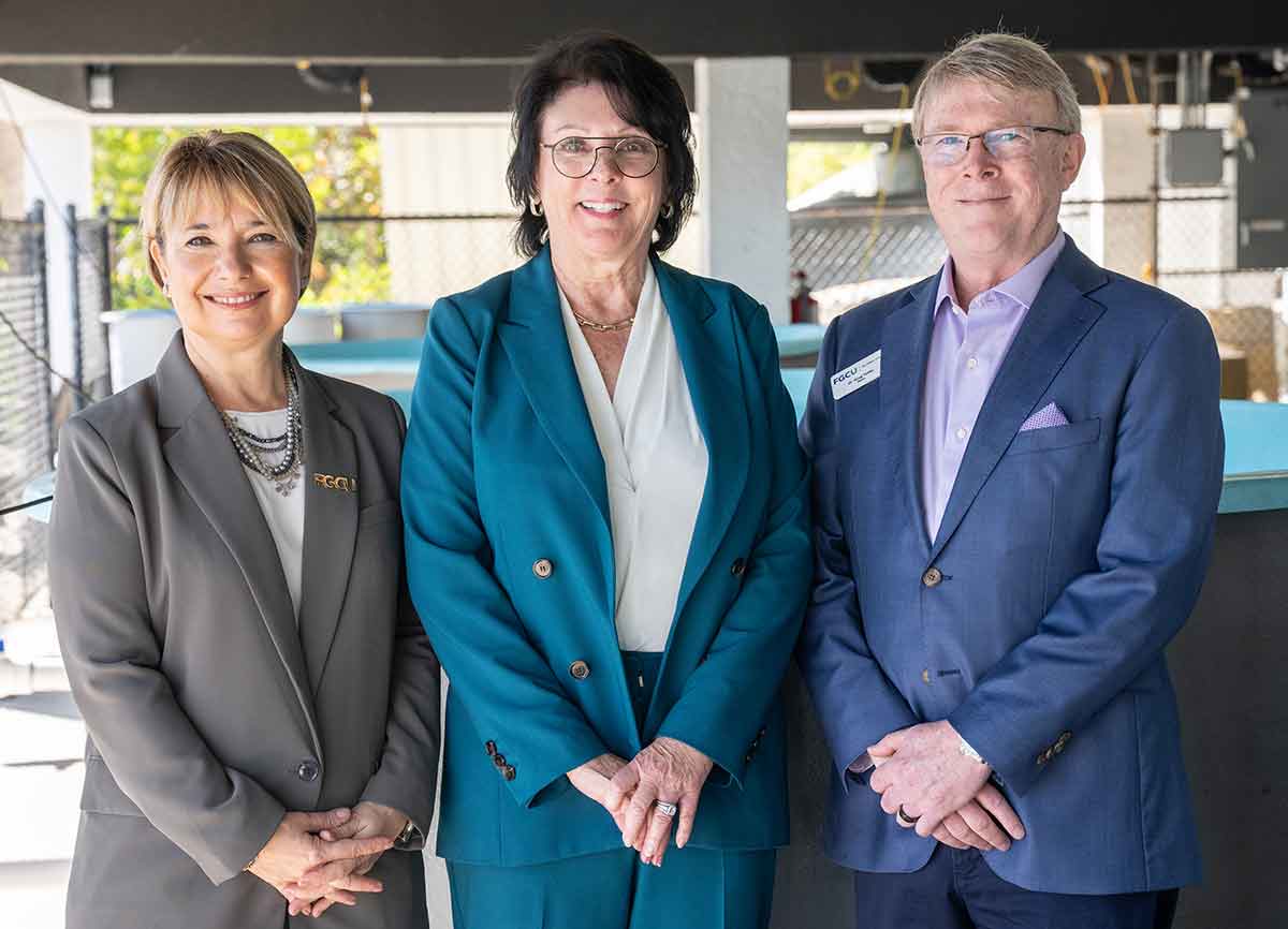 One woman and a man stand smiling, posing for the photographer with their hands clasped in front of each, dressed in business attire