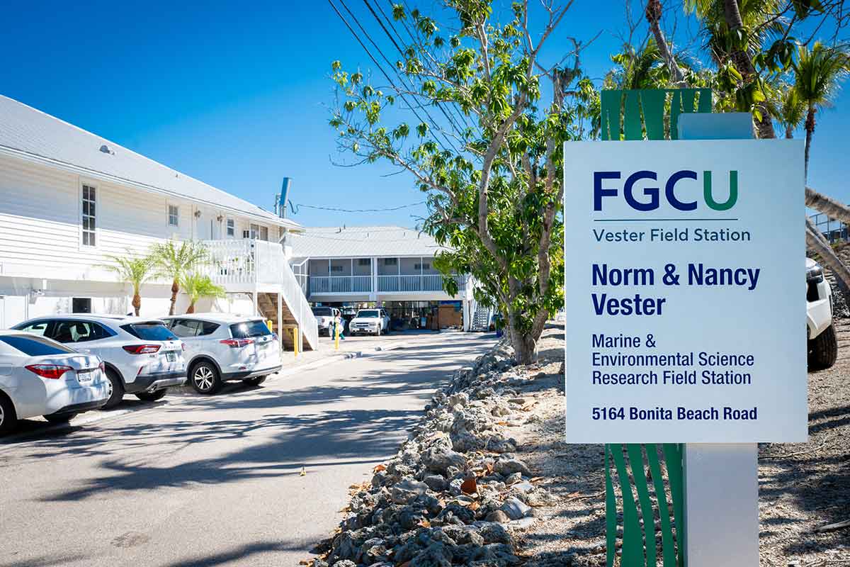 A blue sky frames two white, two-story buildings, a parking lot and a sign that reads FGCU Vester Field Station, Norm and Nancy Vester, Marine and Enviornmental Science Research Field Station, 5164 Bonita Beach Road