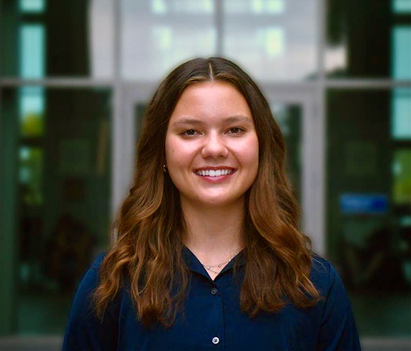 Person standing outside a building with large glass windows in the background.