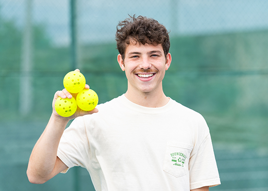 Person holding three yellow pickleballs on a tennis court.