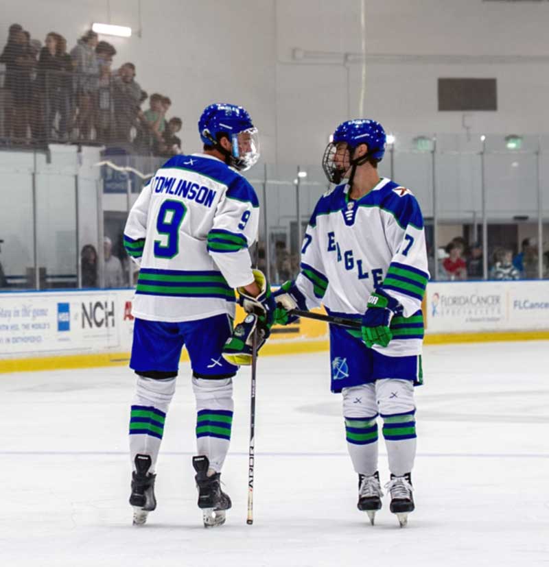 Two hockey players in white and blue jerseys talk on the ice during a game.