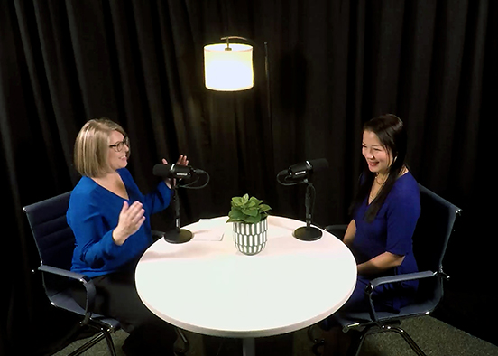 Two people recording a podcast at a round table in a studio with microphones and lights.