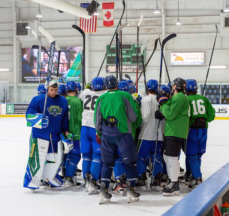 Team huddles on the ice with raised hockey sticks inside an indoor rink.