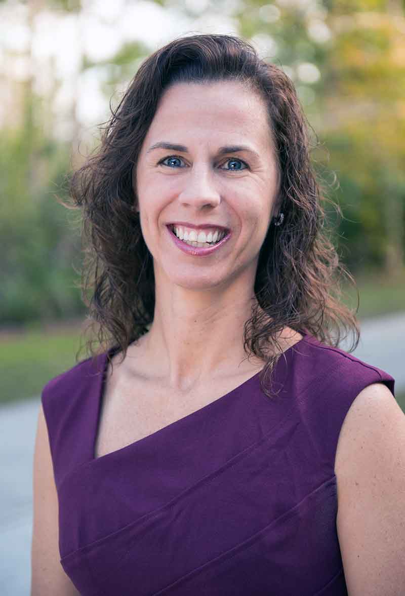 A smiling woman with curly, dark hair in an asymmetrical purple top