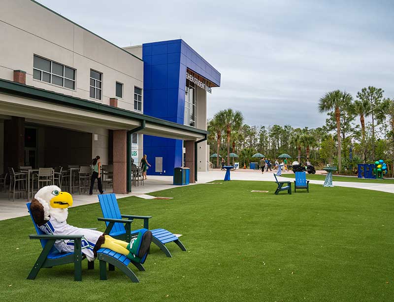 FGCU mascot lounges in chair on green lawn outside campus building