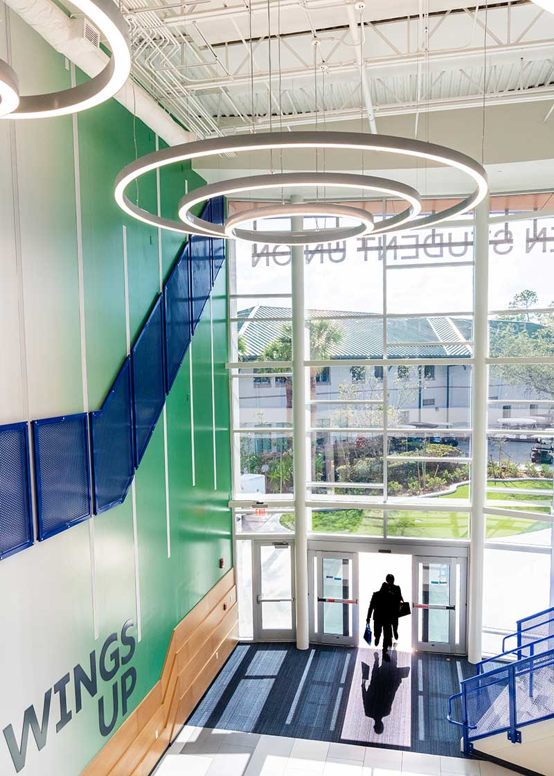 Interior atrium with circular lights, Wings Up wall, and person entering.